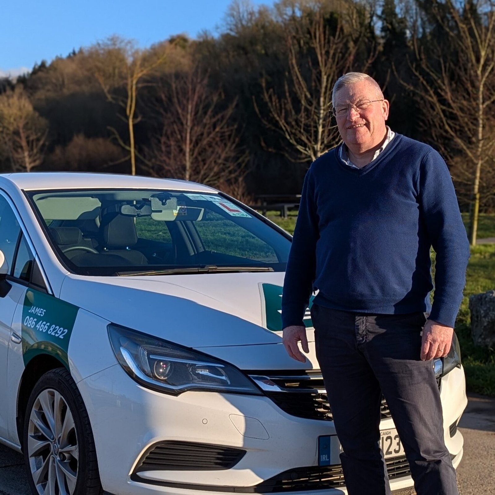 James Flynn standing beside the white school car with his name and mobile on the door