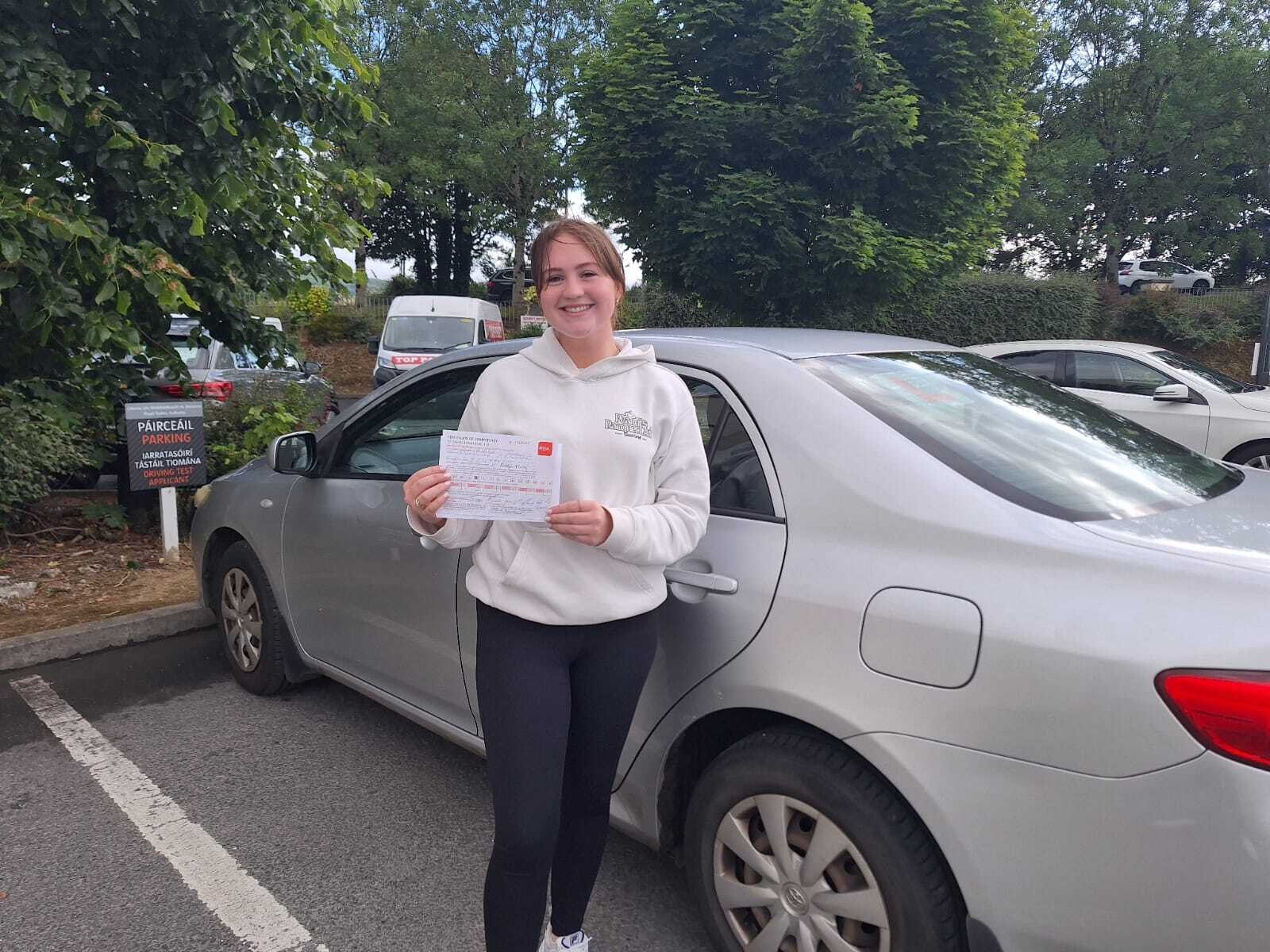 A newly qualified driver with an RSA pass certificate at a driving test centre car park